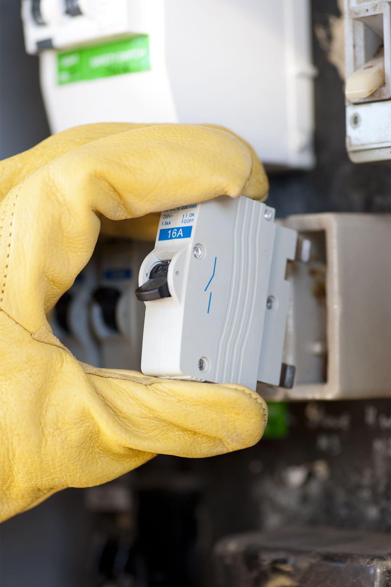 A person wearing yellow gloves is holding a circuit breaker in their hand