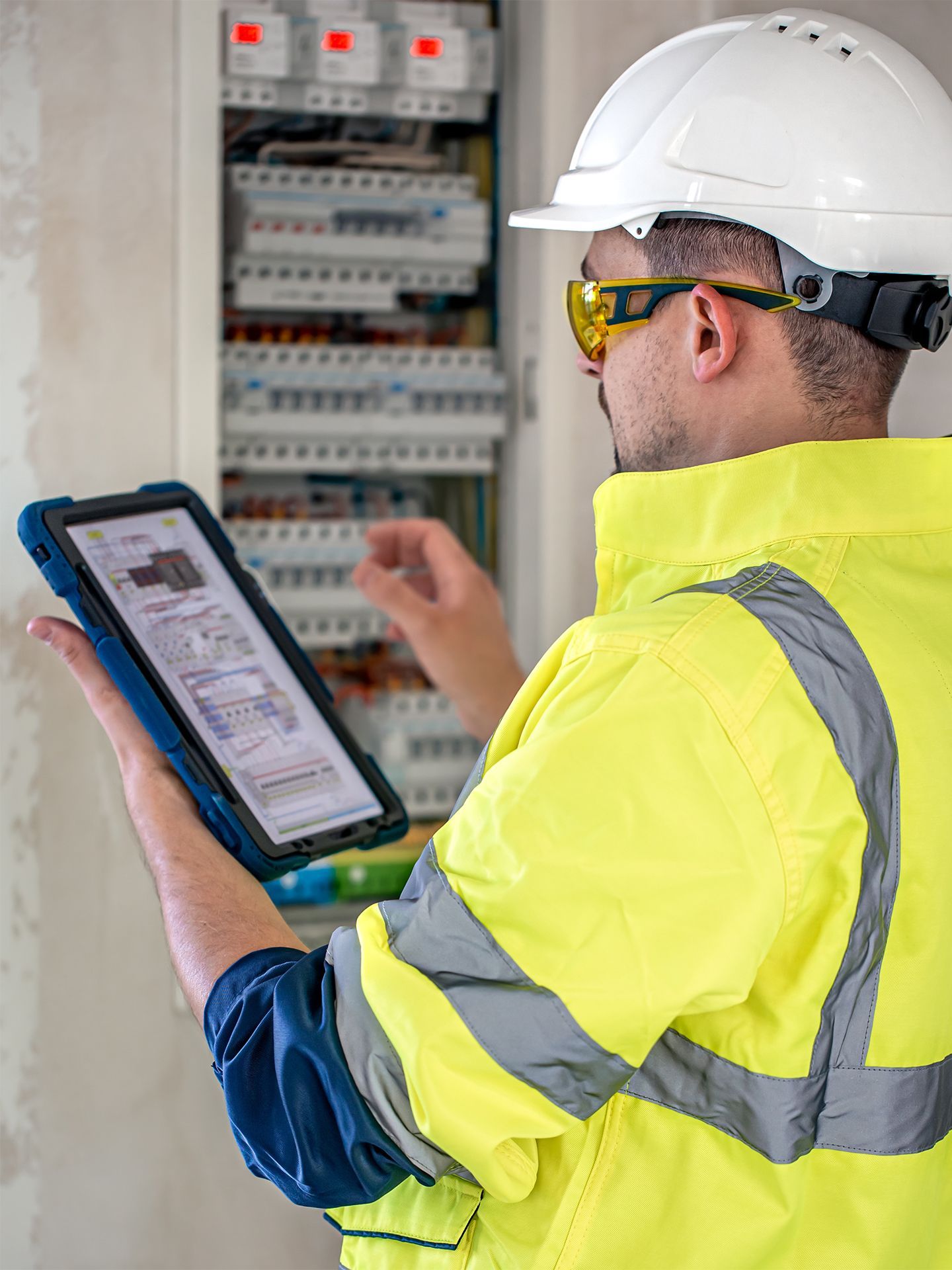 A man wearing a hard hat and safety vest is looking at a tablet