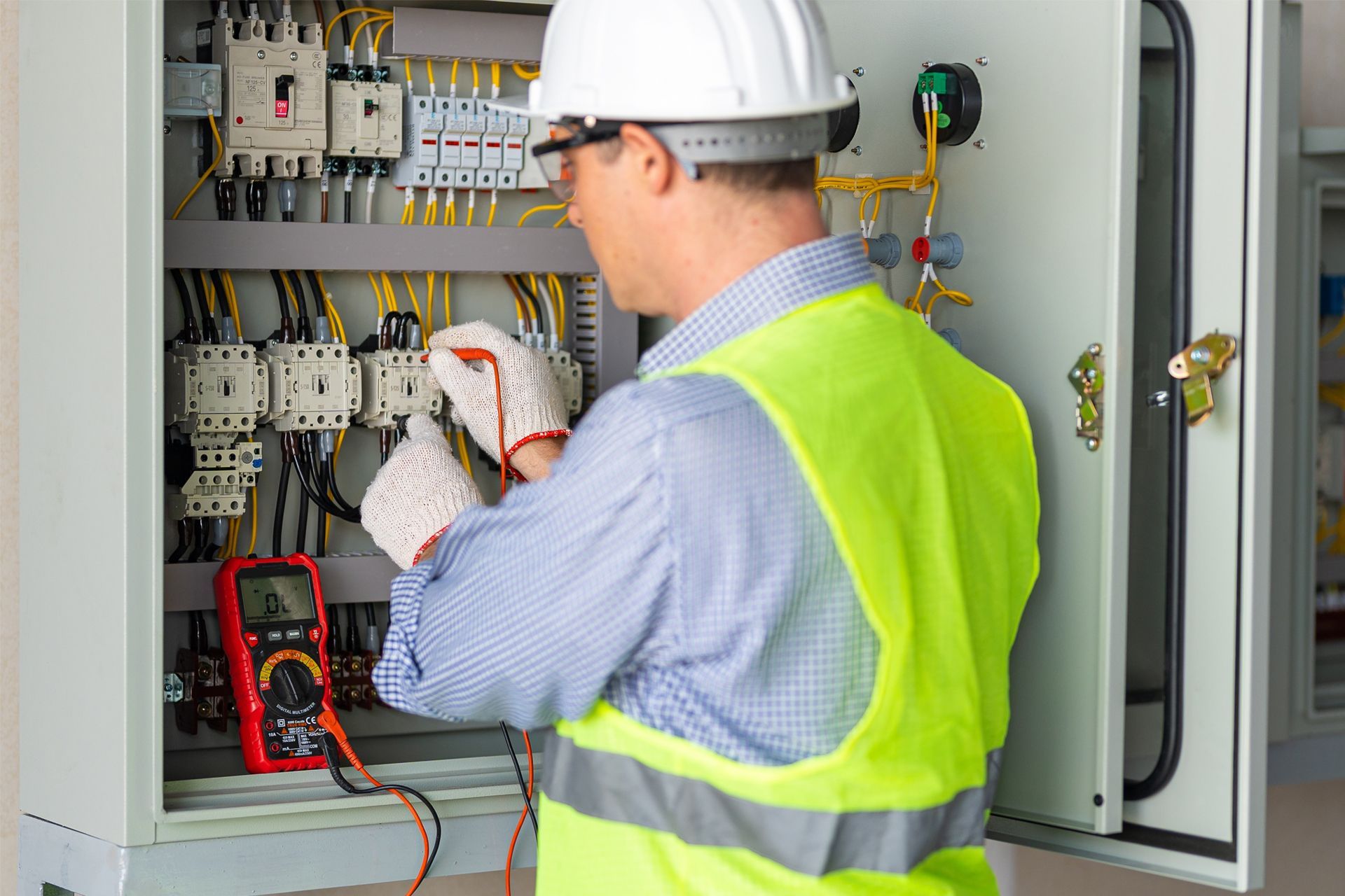 A man in a hard hat and safety vest is working on an electrical box