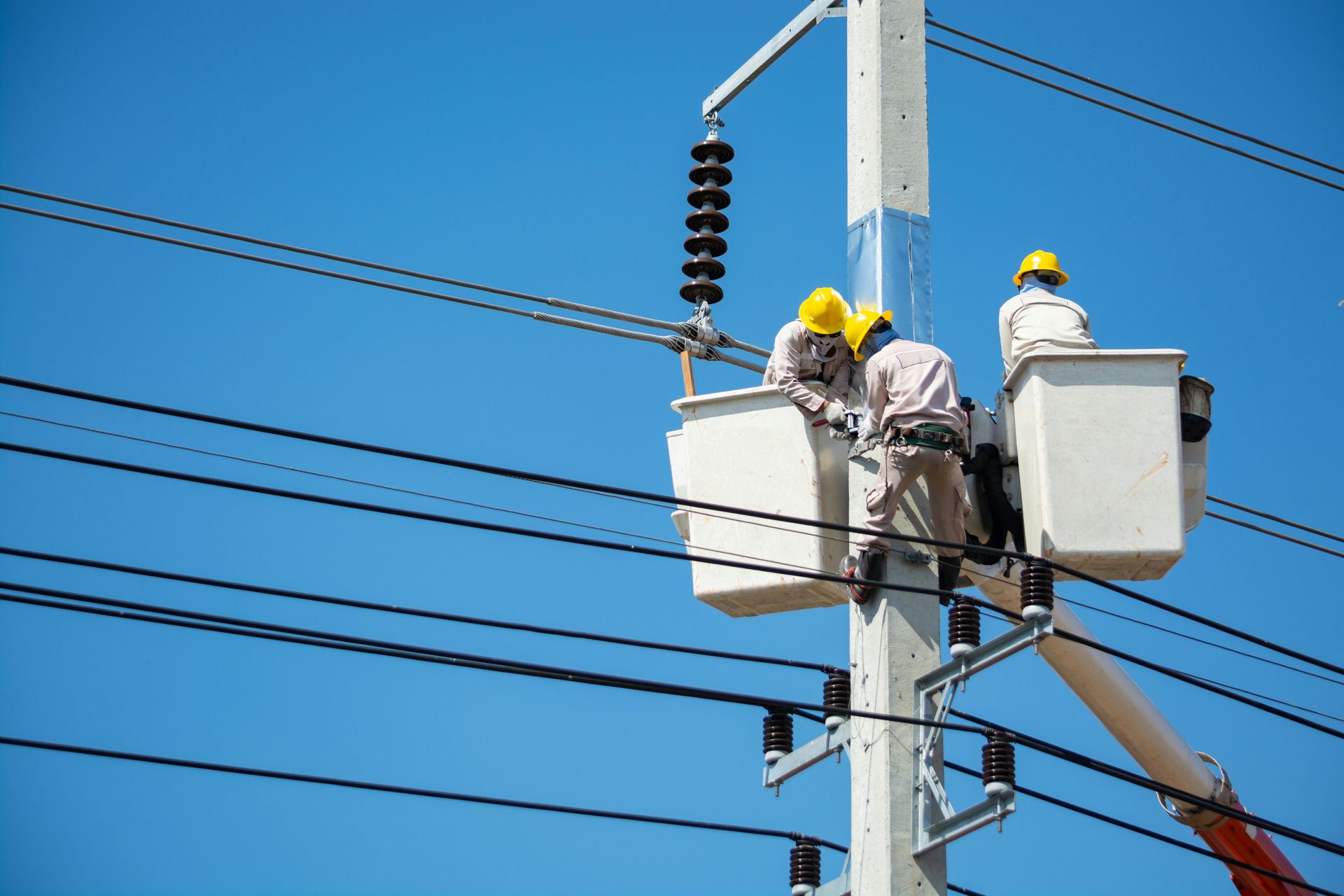Utility workers in yellow helmets repairing power lines from bucket lifts