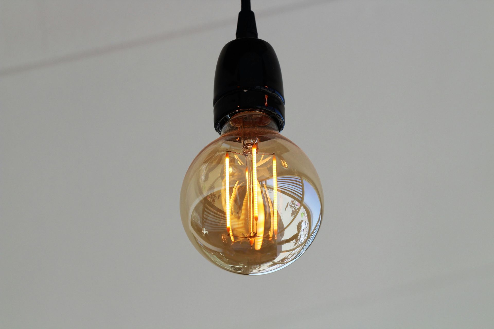 A round, amber-tinted Edison-style LED light bulb glows warmly, hanging from a simple black socket against a white ceiling.