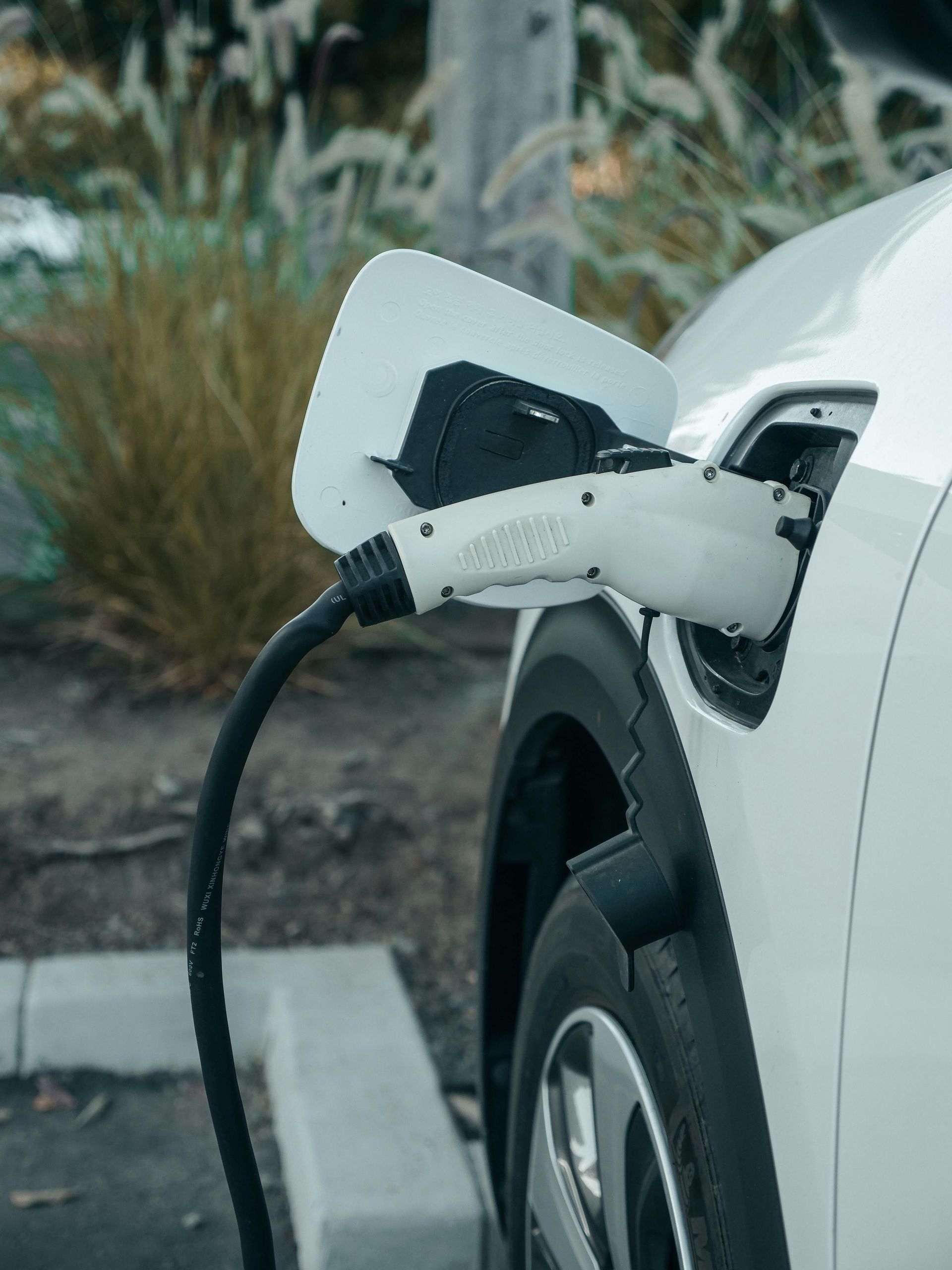 Electric vehicle charging cable plugged into a white car at a roadside charging station.