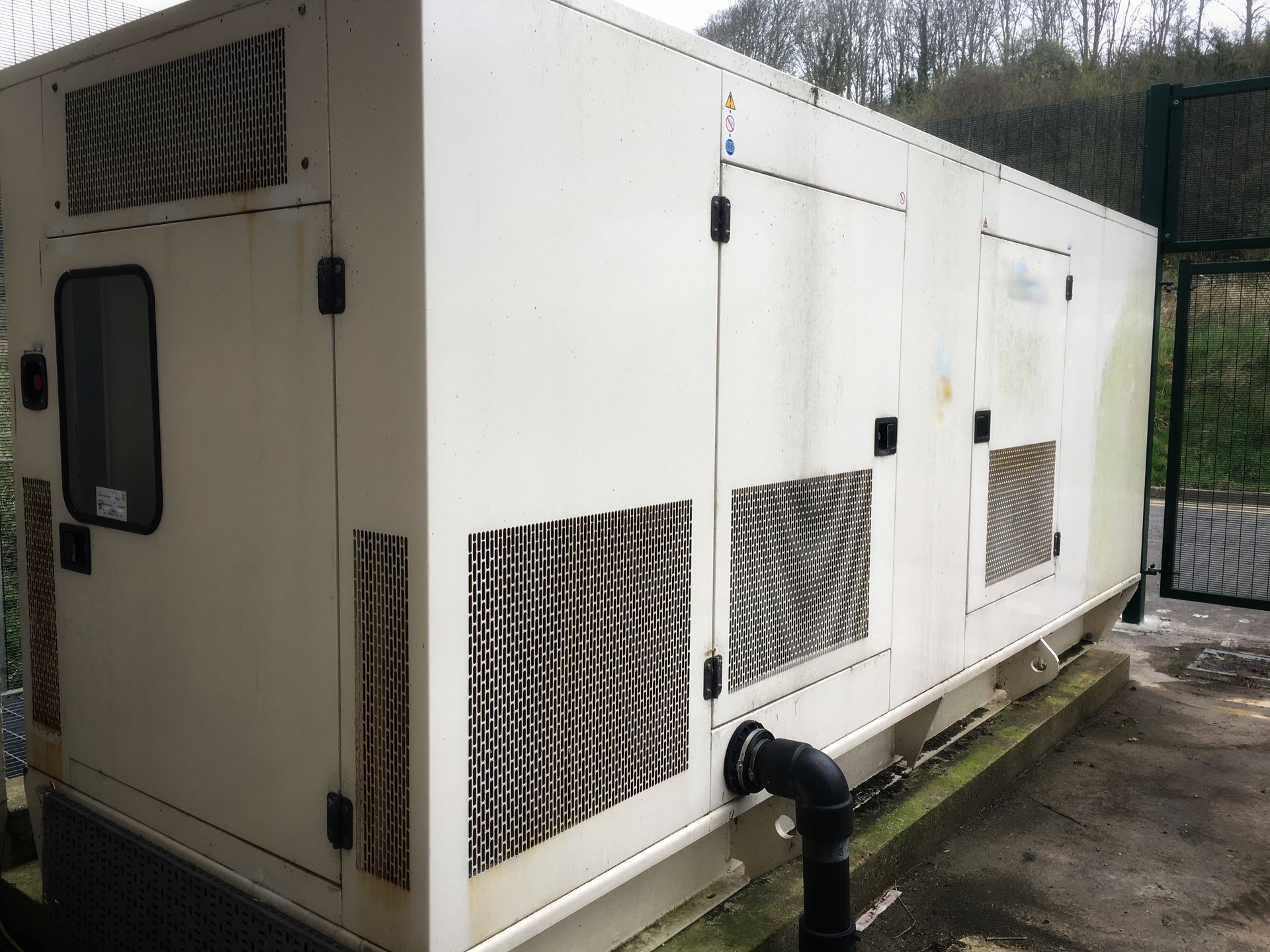 White industrial generator container with vents and pipes outdoors on concrete pad