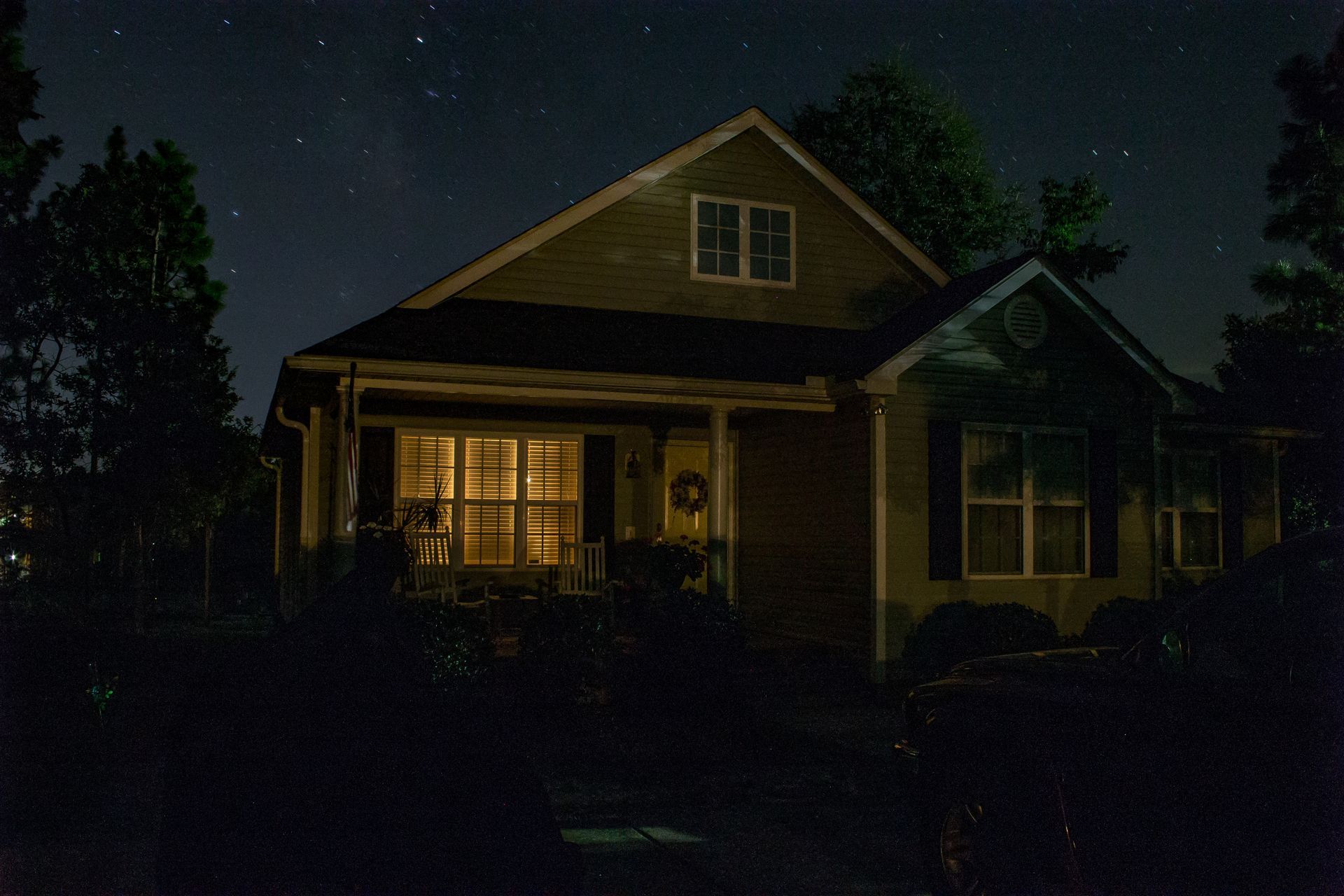 Dimly lit house at night with warm lights glowing from the porch and windows.