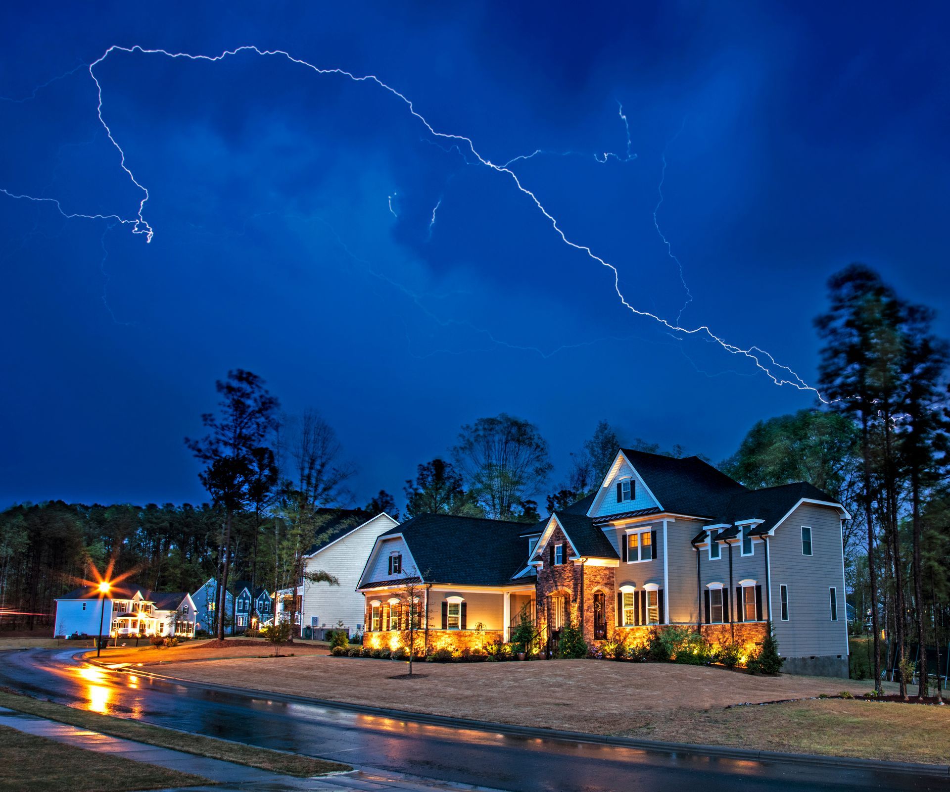 Lightning over a lit house on a rainy street at dusk