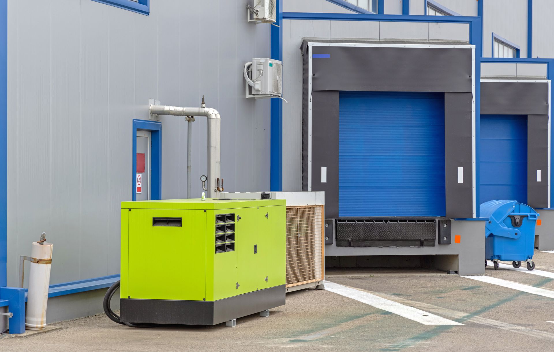 Industrial loading dock with blue doors, a green generator, and a blue cart outside a warehouse