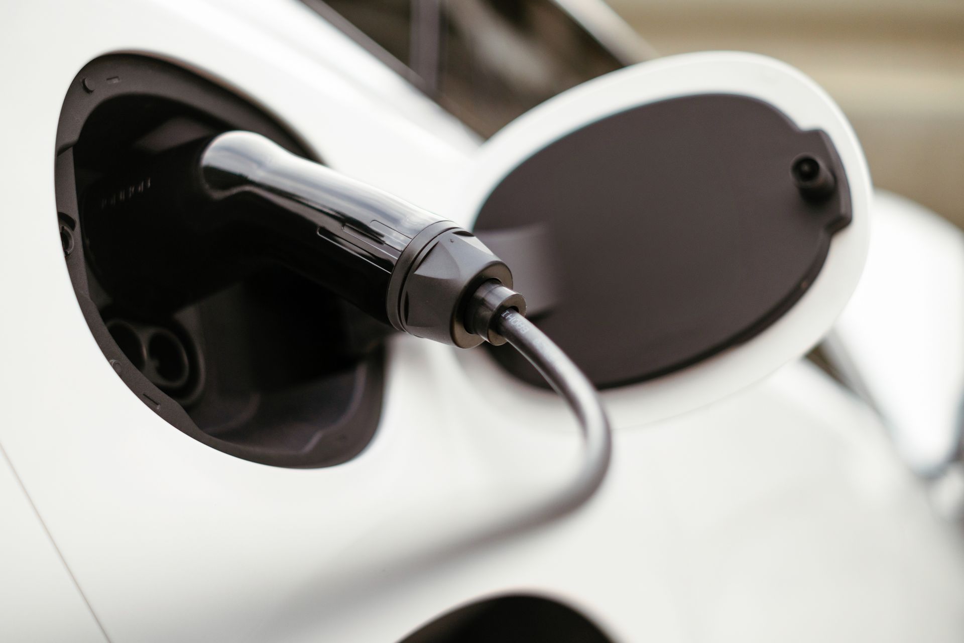 White electric car being charged with a black charging cable.