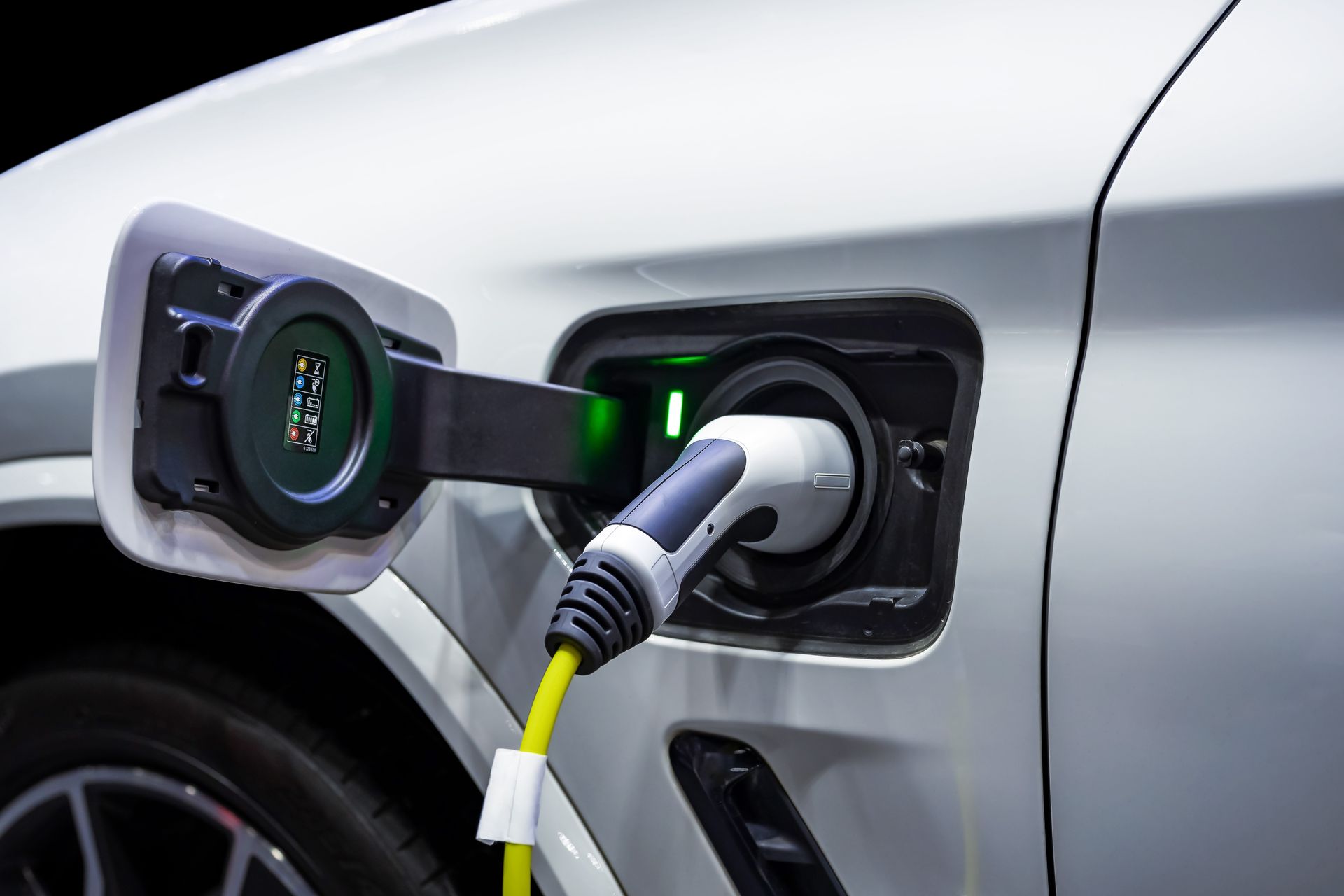 Electric car charging port with a cable plugged into a white vehicle