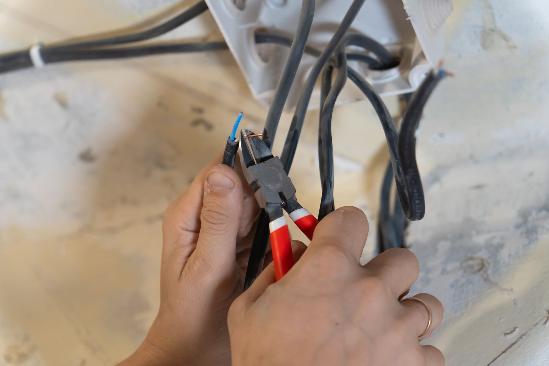 Hands using wire cutters to strip electrical wires on a work surface.