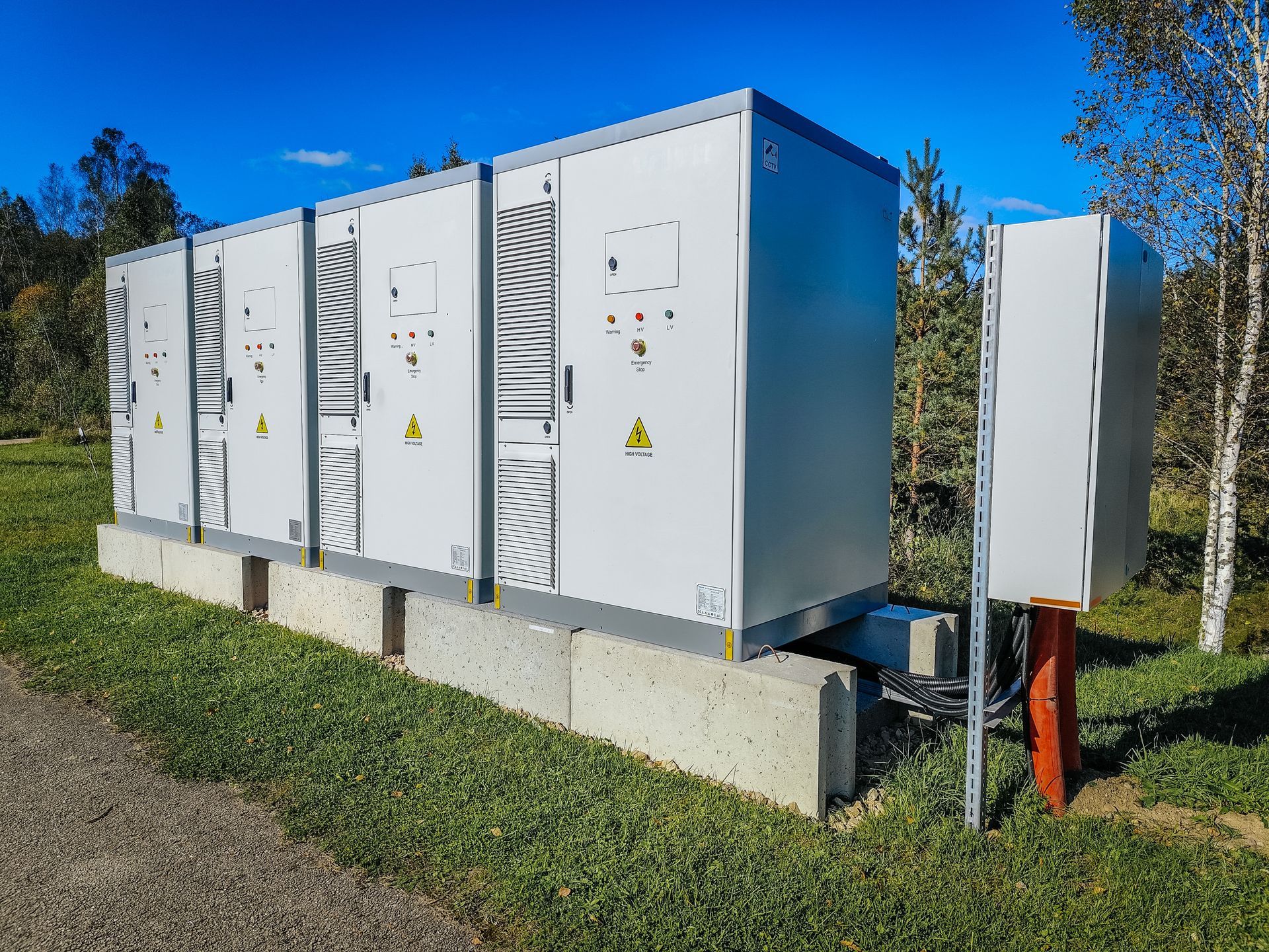 Gray electrical control cabinets on a concrete pad outdoors, with trees and blue sky in the background