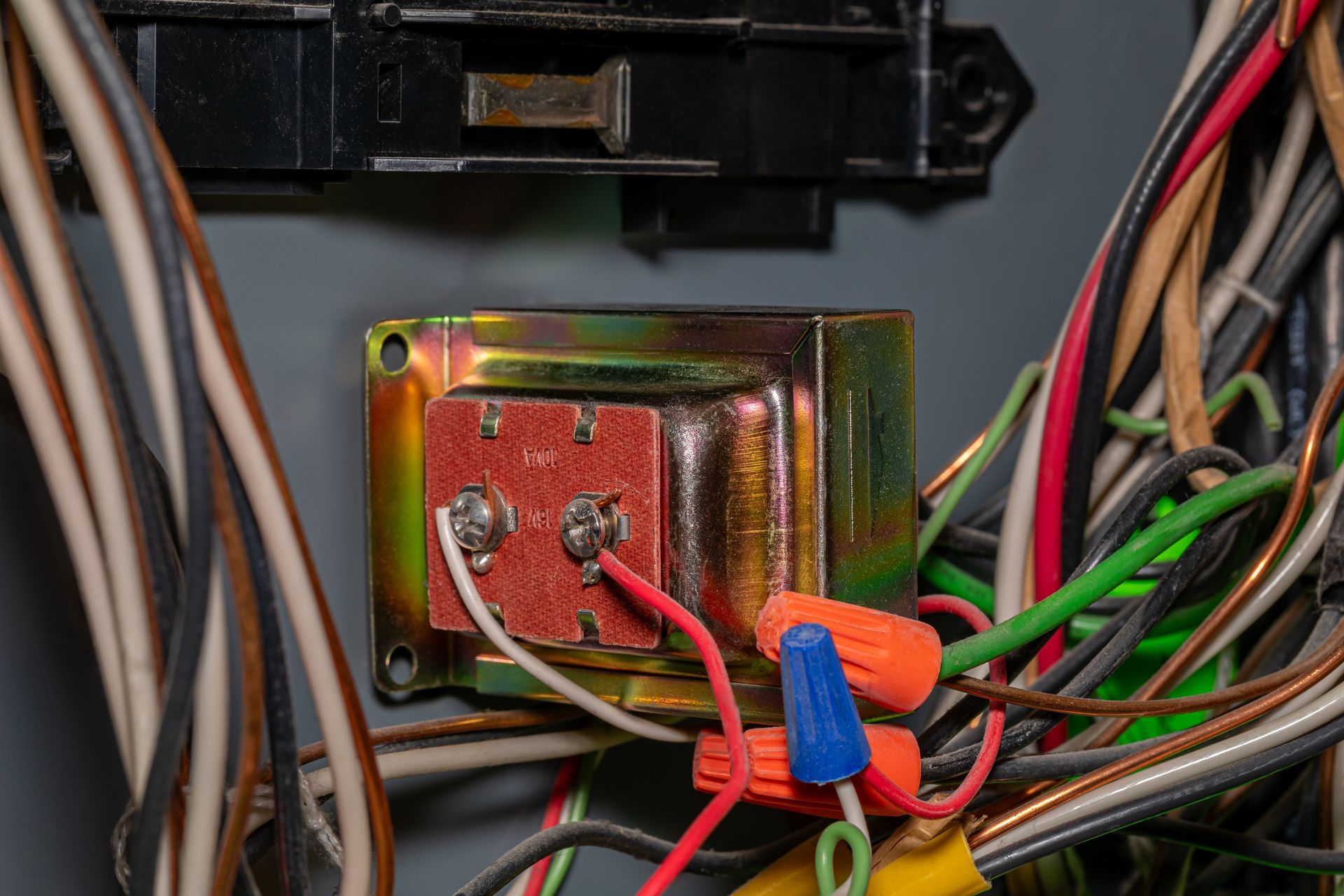 Close-up of a metal electrical terminal with red and green wires connected inside a device panel