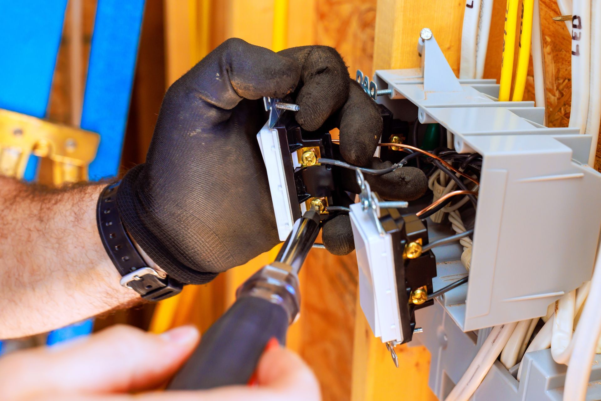 Person with black gloves using a screwdriver to install electrical switches in a wall.