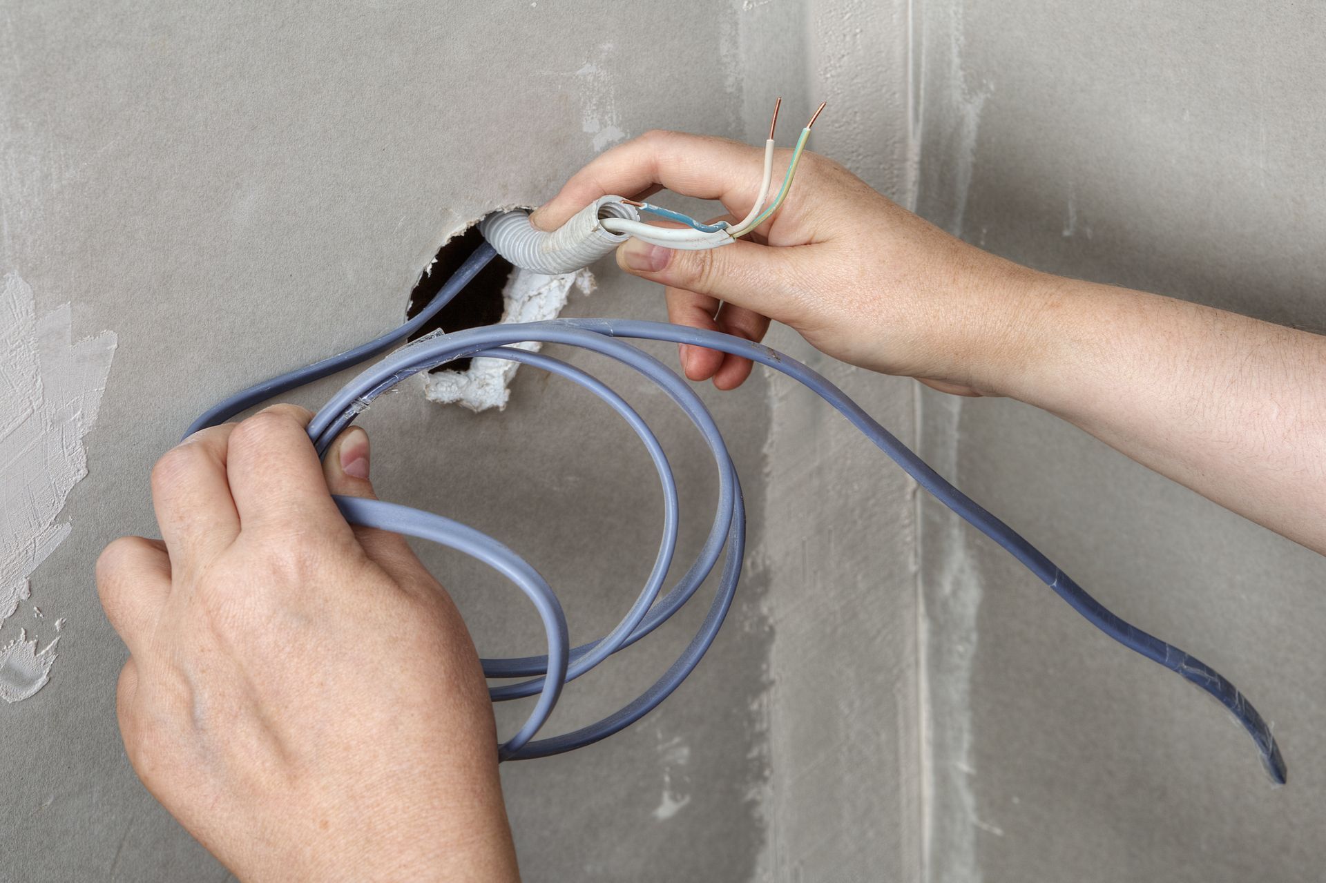 Hands wiring a wall outlet with blue electrical cables exposed and connected