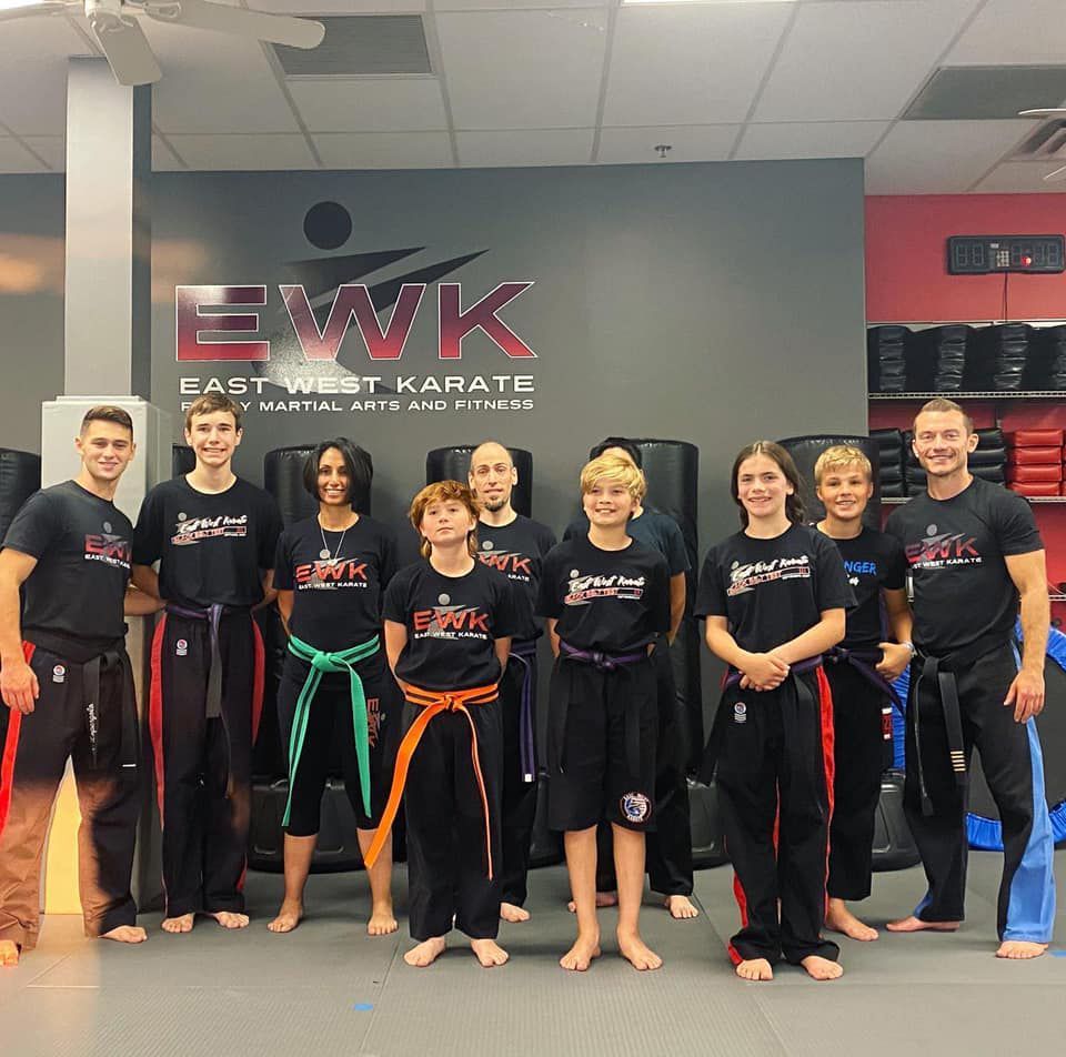 a group of people posing for a picture in front of a sign that says east west karate