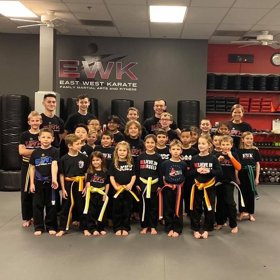a group of kids are posing for a picture in front of a sign that says east west karate
