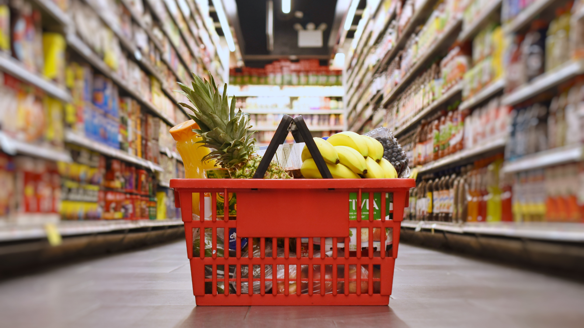 A red shopping basket filled with fruits and vegetables in a grocery store