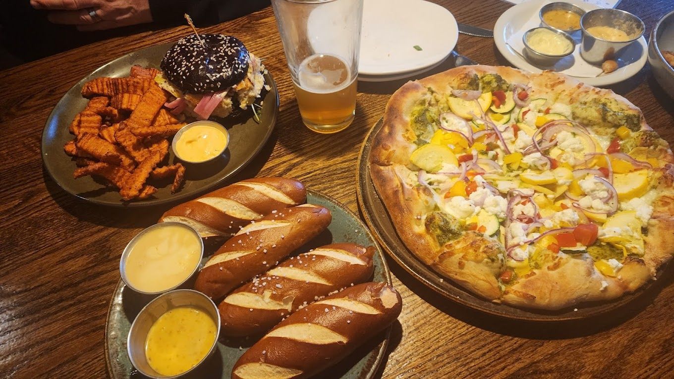 A table topped with plates of food including pretzels and a pizza Grizzly Peak Restaurant Ann Arbor MI