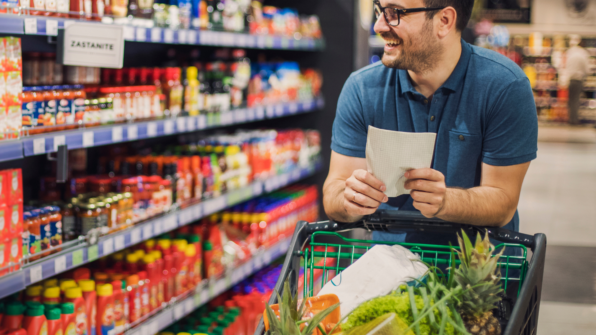 A man is looking at a shopping list while shopping in a grocery store.