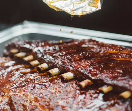 A close up of a tray of ribs with sauce being poured over them Ricewood BBQ Ann Arbor MI