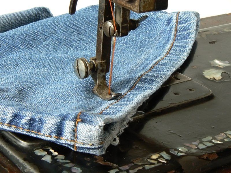 A sewing machine is stitching a piece of blue jeans