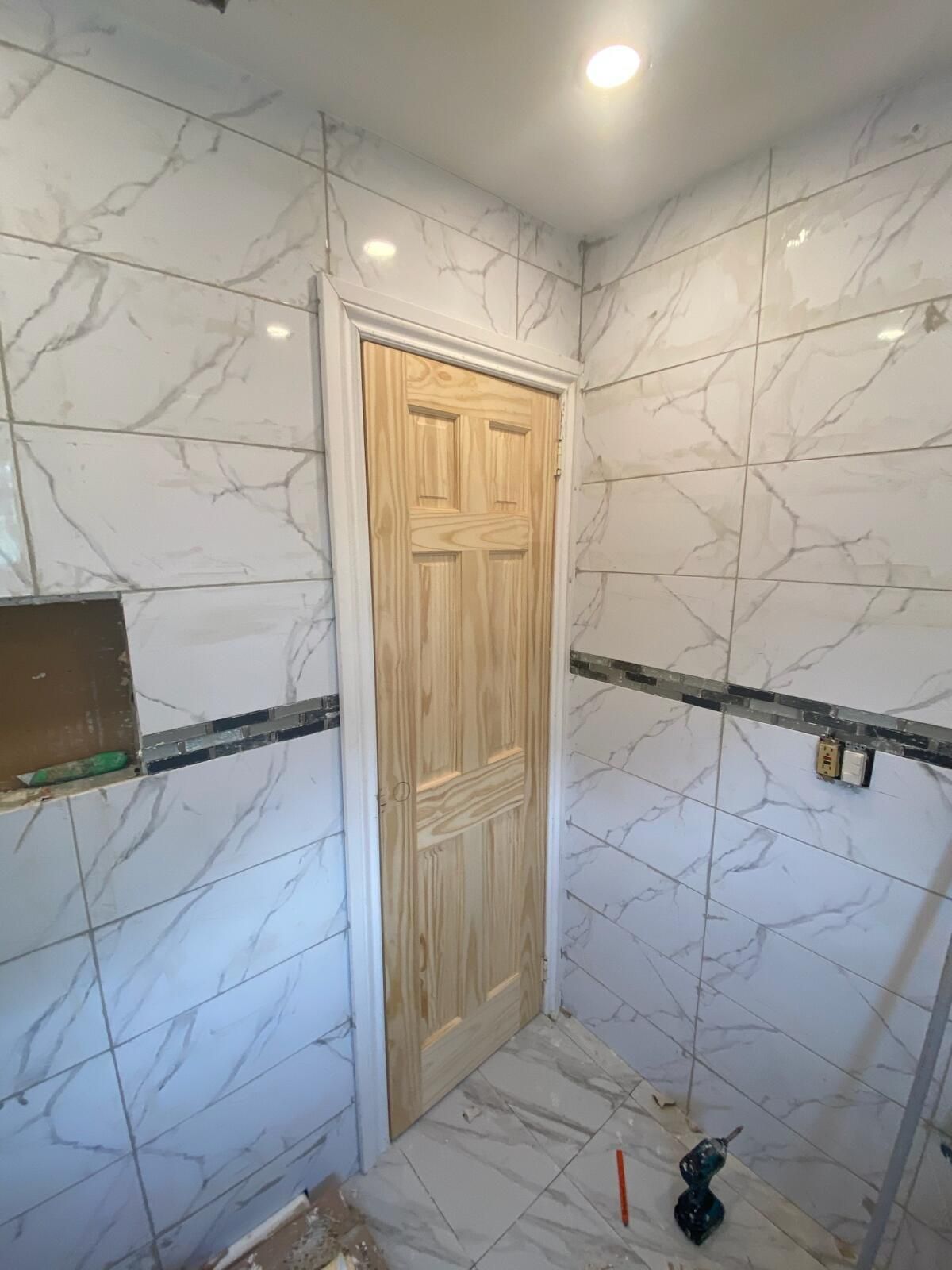 A bathroom with white tiles and a wooden door.
