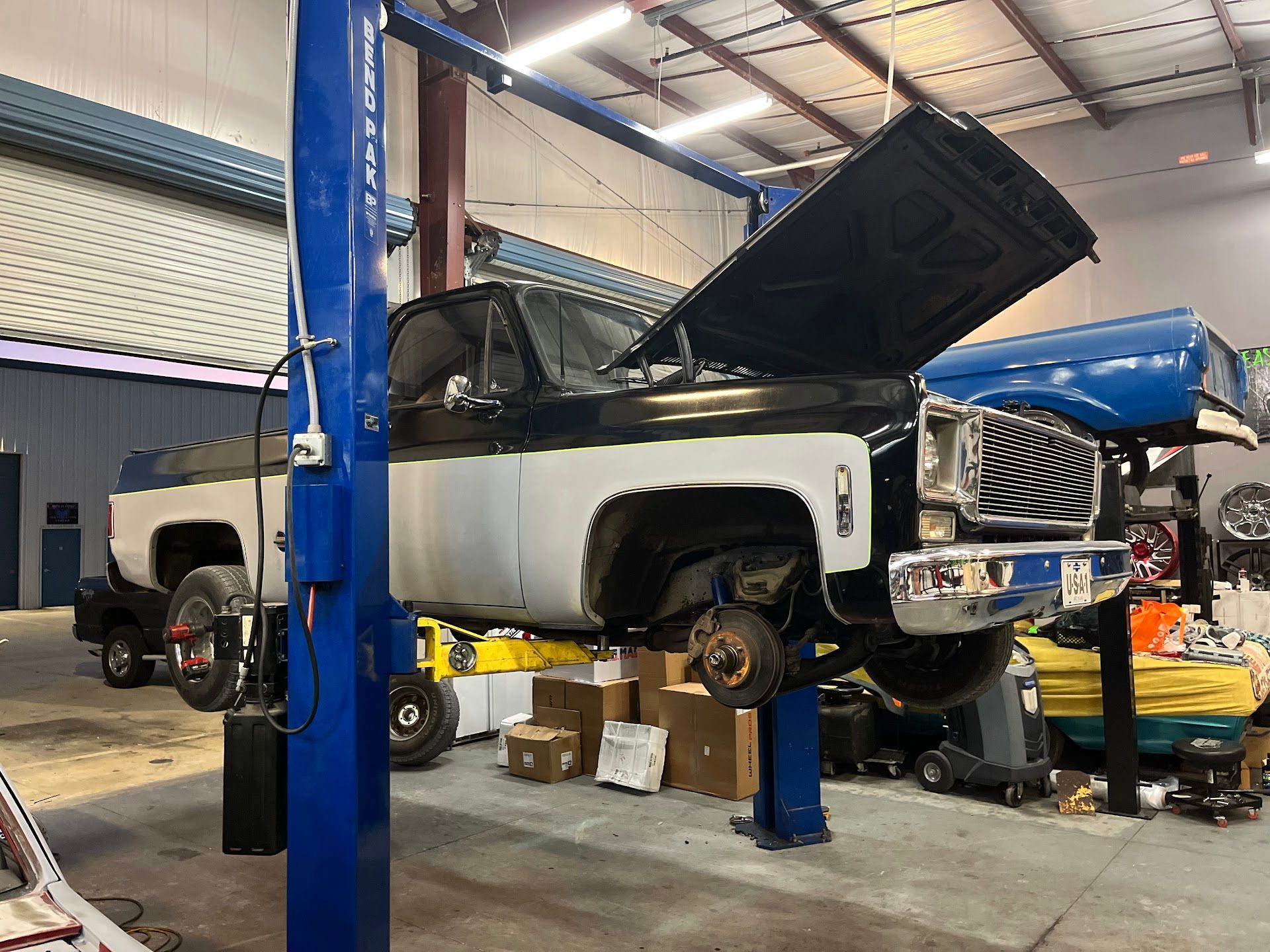 Classic truck raised on a lift in a garage, hood open. White and black paint, wheels removed. | East Coast Motorworks