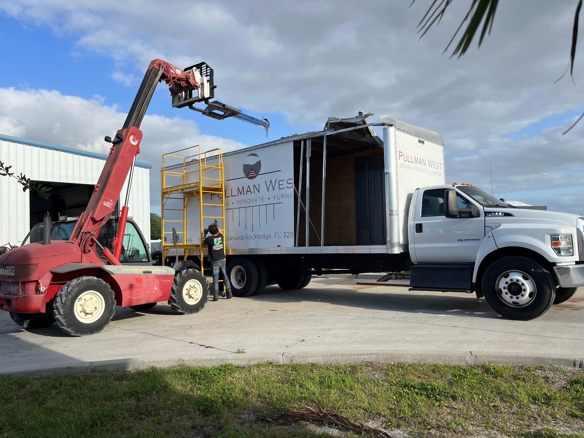 A red forklift with a white box truck. A worker stands near the truck. Outdoors, day. | East Coast Motorworks