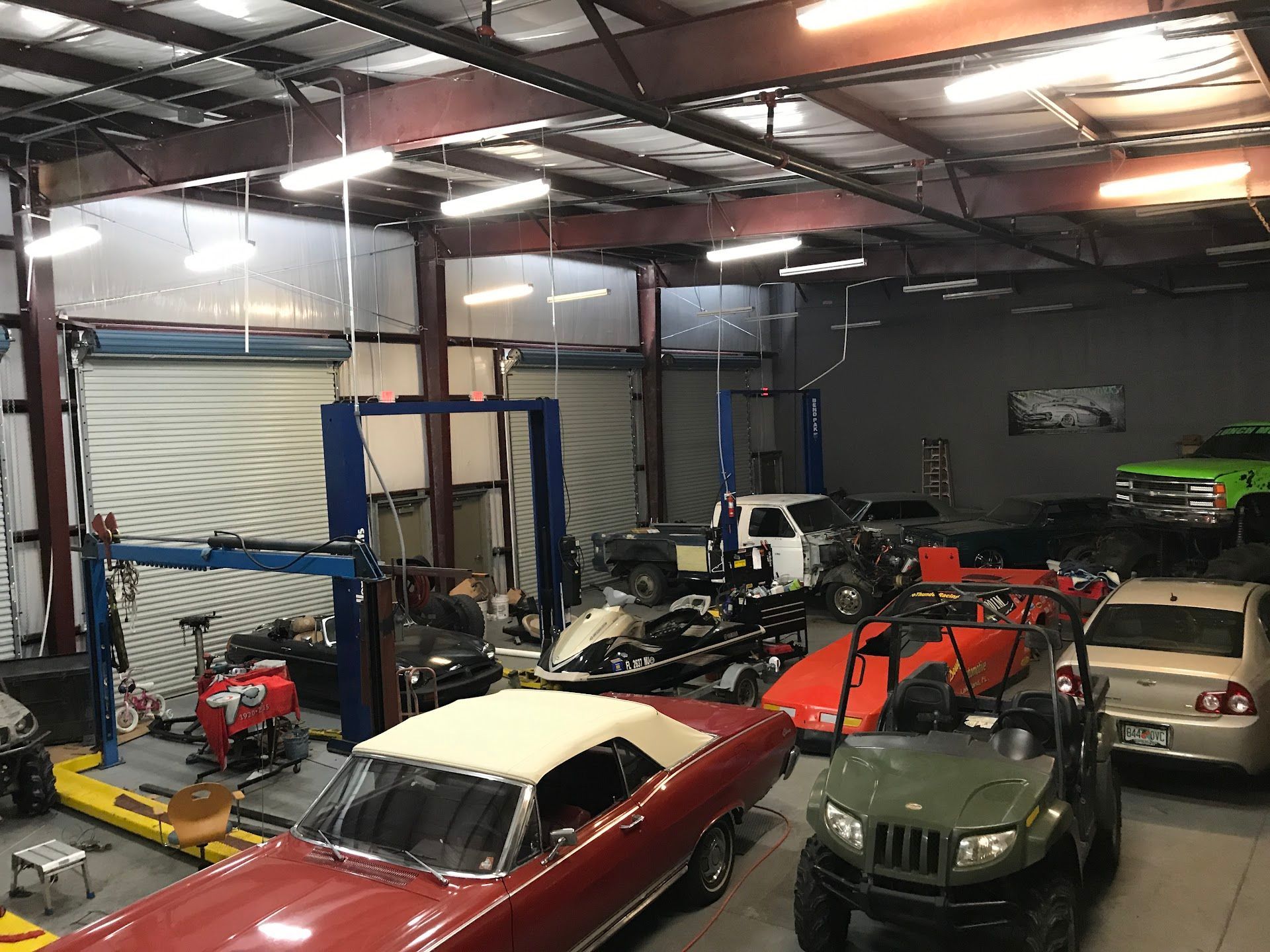 A well-lit auto repair shop with multiple vehicles, including a red convertible and a green SUV, on lifts. | East Coast Motorworks