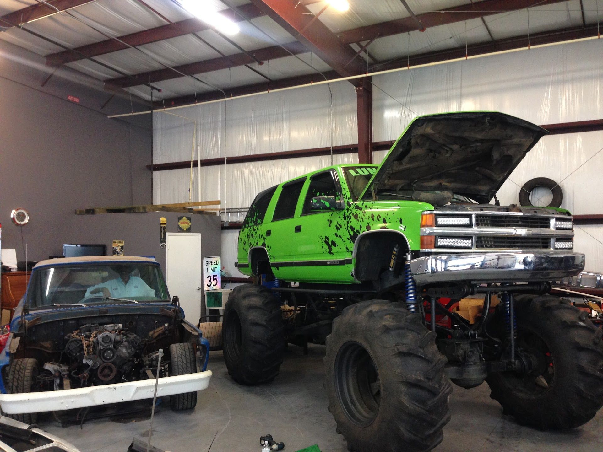 Green monster truck in a garage with a pickup truck. | East Coast Motorworks