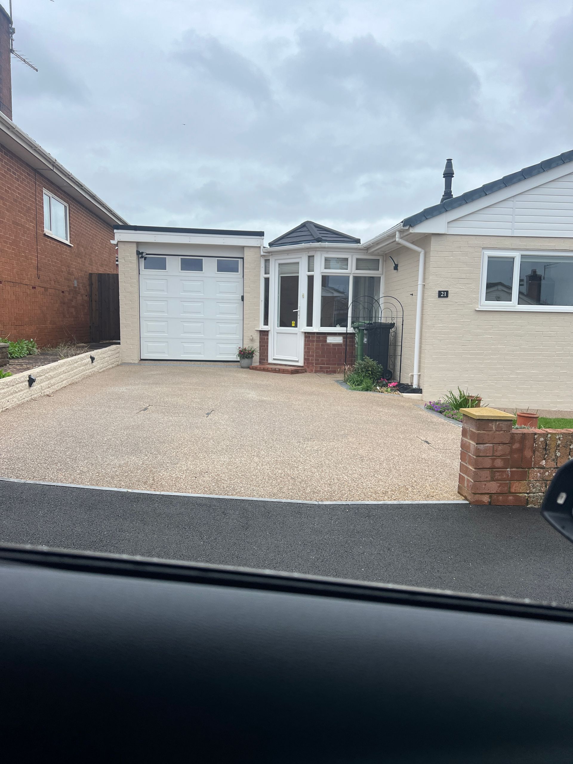 Light beige resin driveway leading up to a white garage and cream bungalow.