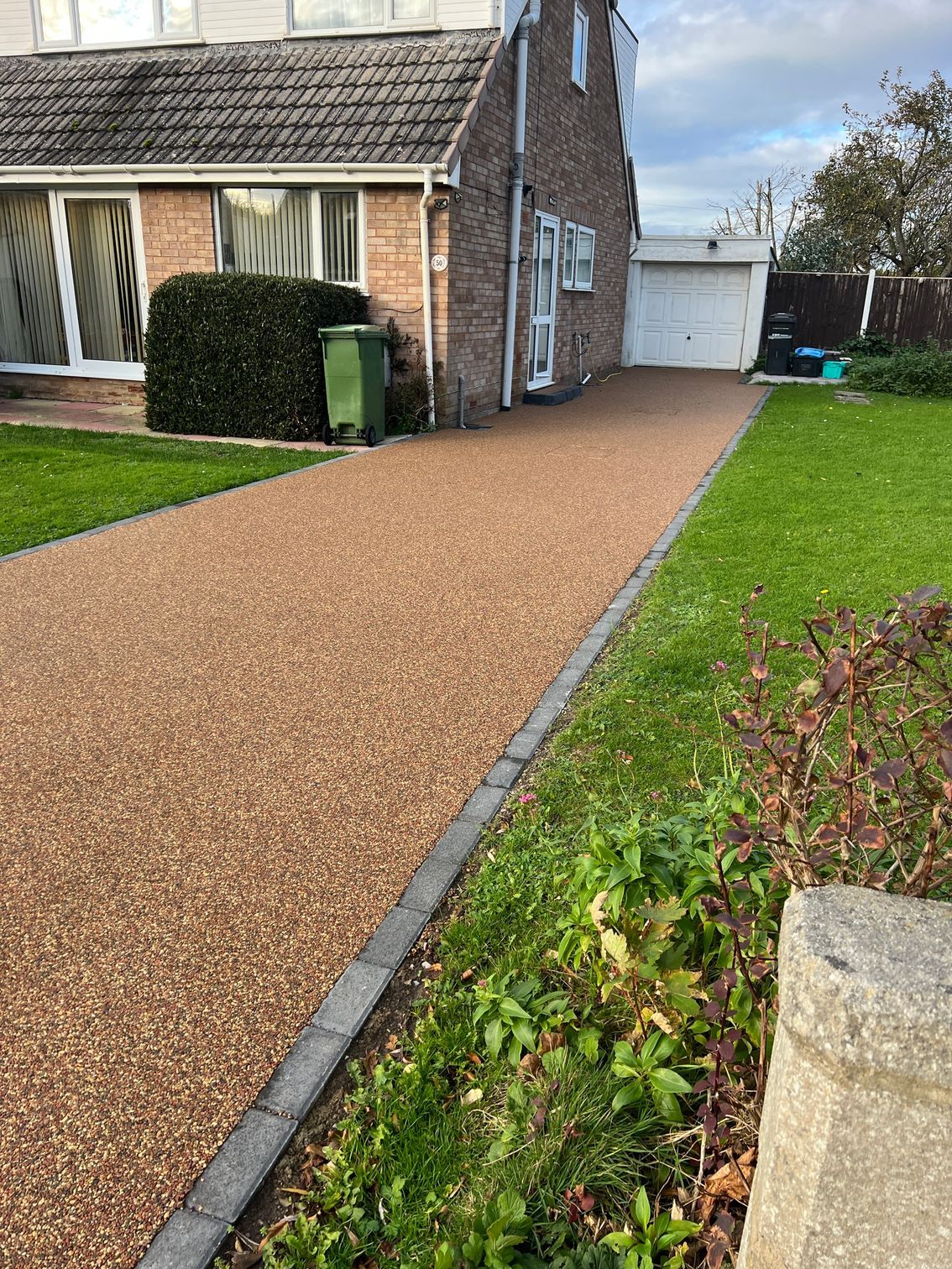 Resin driveway between 2 patches of grass, leading up to a white garage