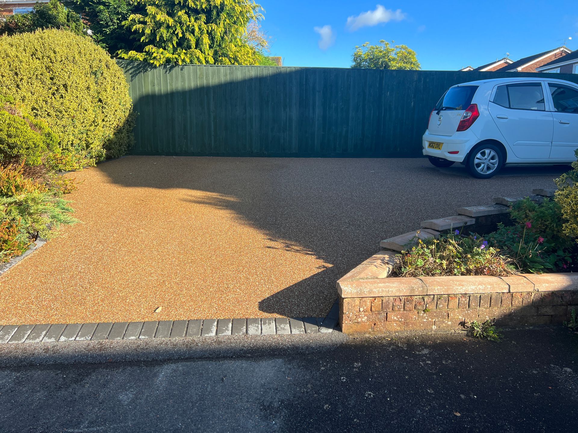 Light brown resin driveway with a white car parked on it.