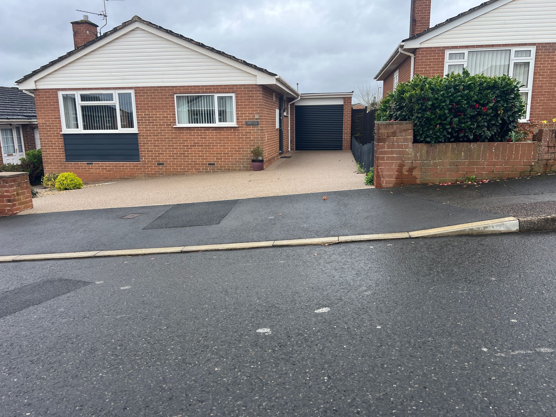 Small beige resin driveway installed outside a red brick bungalow.