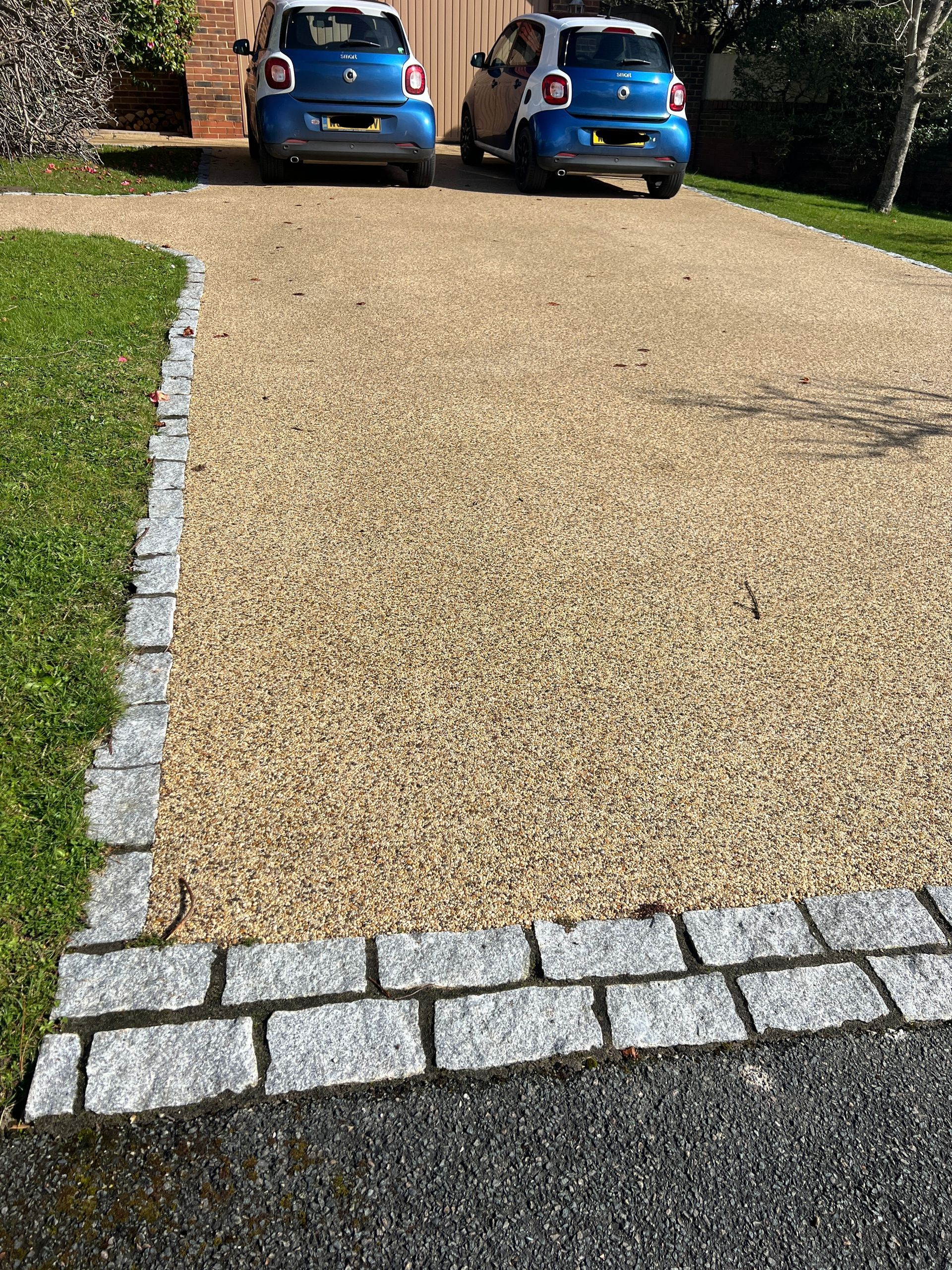 Light beige resin driveway with grey block paving bored, surrounded by grass.