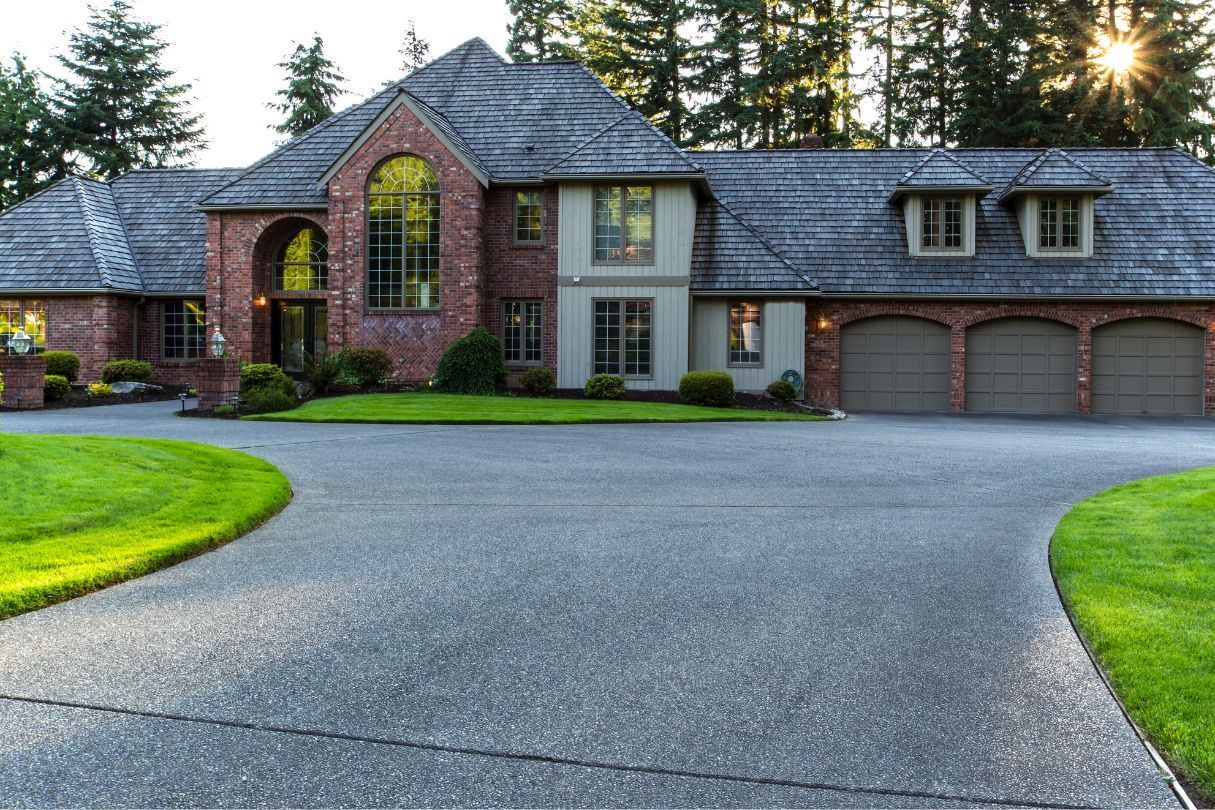 Perfect grey resin driveway surrounded by rich green grass, leading up to a large mixed brick home