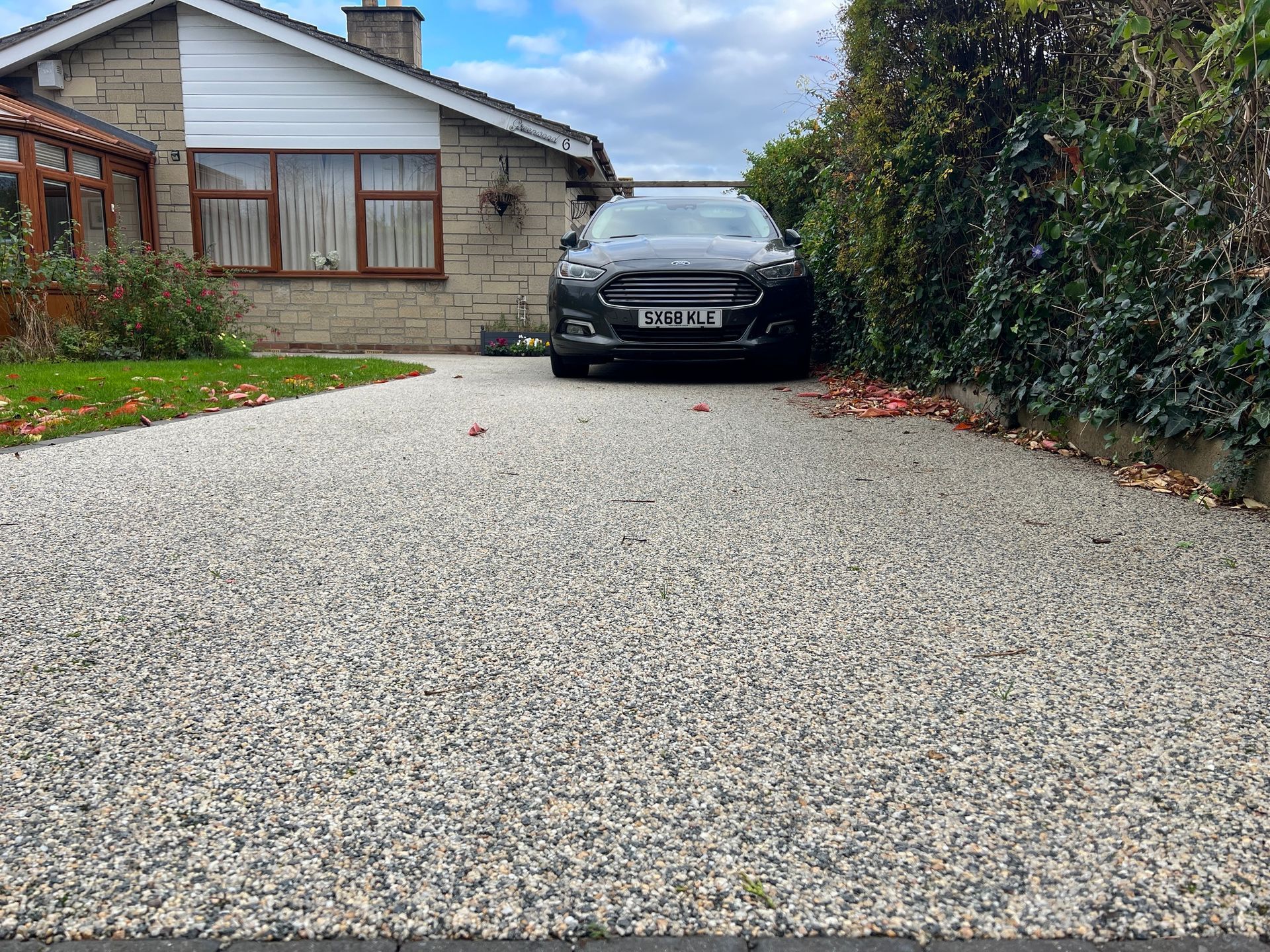 Grey resin driveway leading up to a grey bungalow, with a car parked at the top of the drive.