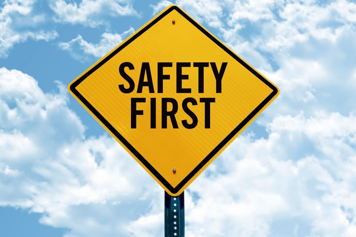 Safety first sign, with black writing and a yellow background. Behind the sign is a cloudy sky.