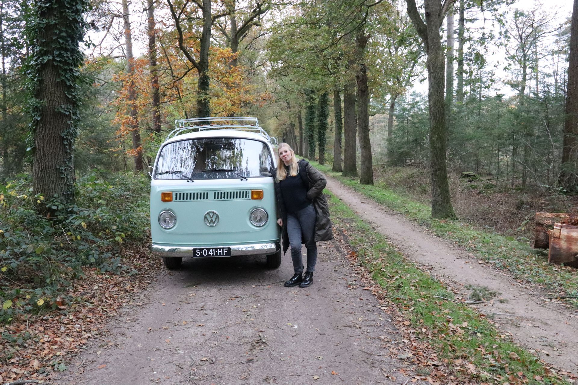 Een vrouw staat naast een busje op een onverharde weg in het bos.