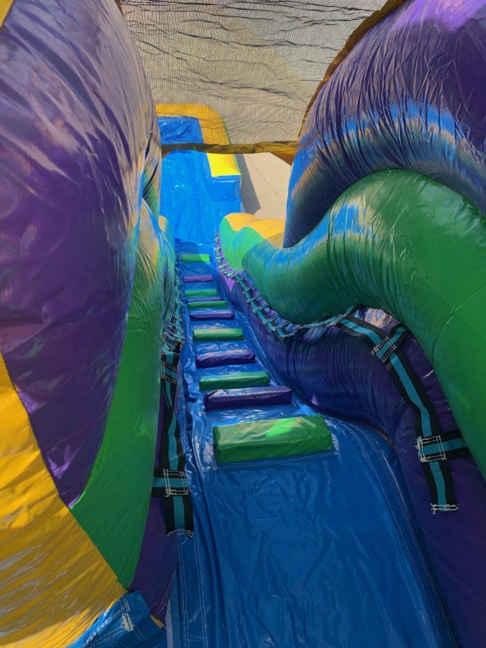 A purple , green and yellow inflatable water slide with stairs going down it.