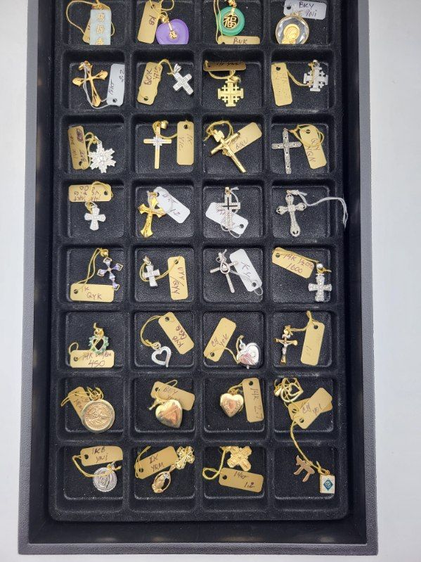 A tray of small pendants, mostly crosses, hearts, and tags, in gold and silver colors.