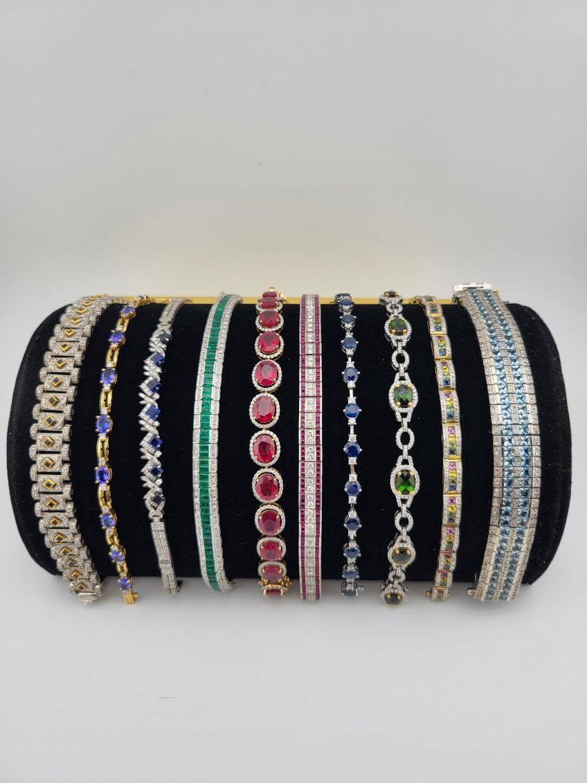 Assortment of jeweled bracelets of various designs and colors displayed on a black velvet cylinder.