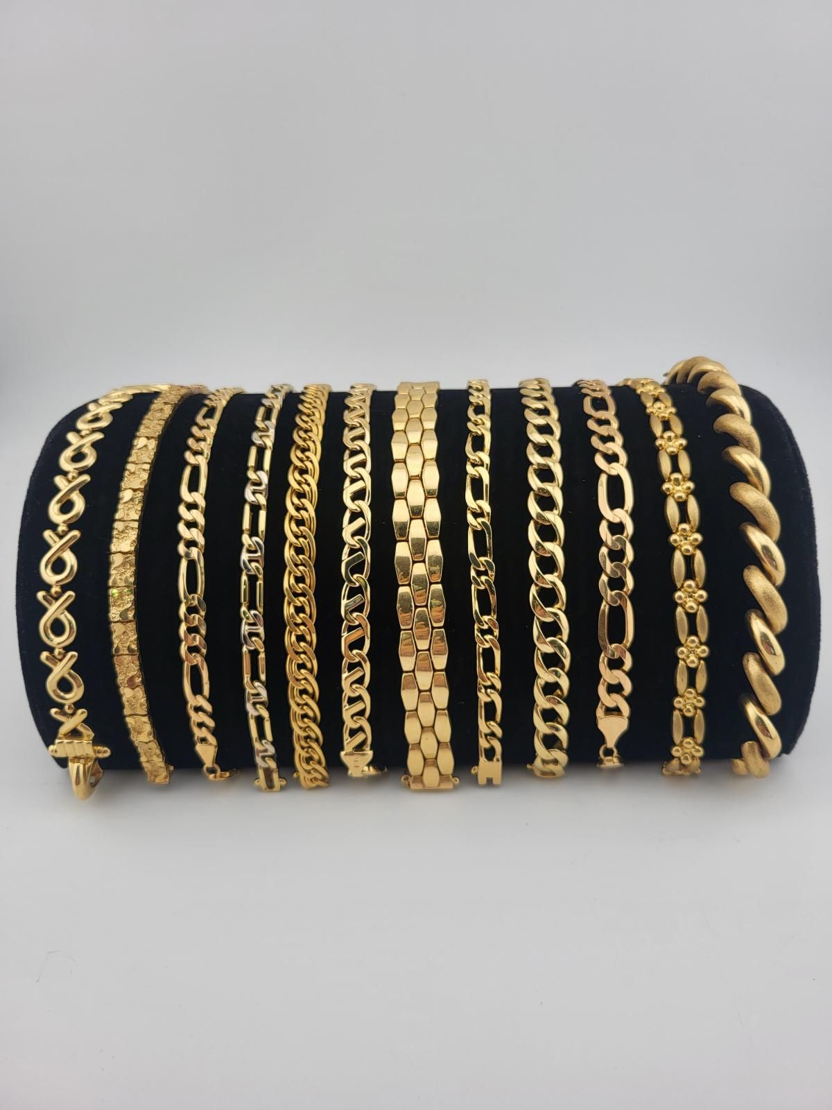 Gold bracelets displayed on a black cylindrical stand against a white background.