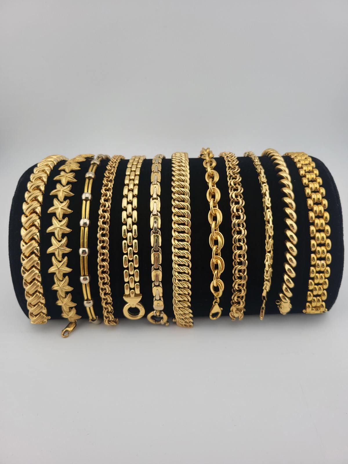 Gold bracelets displayed on a black cylindrical stand against a neutral backdrop.