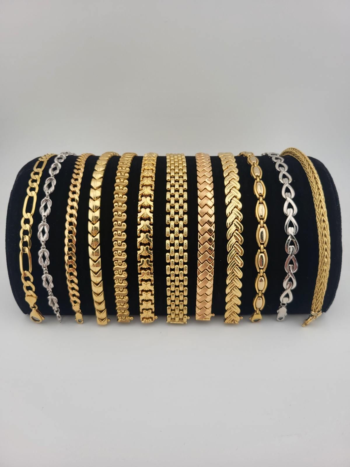 Assortment of gold bracelets displayed on a black cylindrical pillow against a white background.