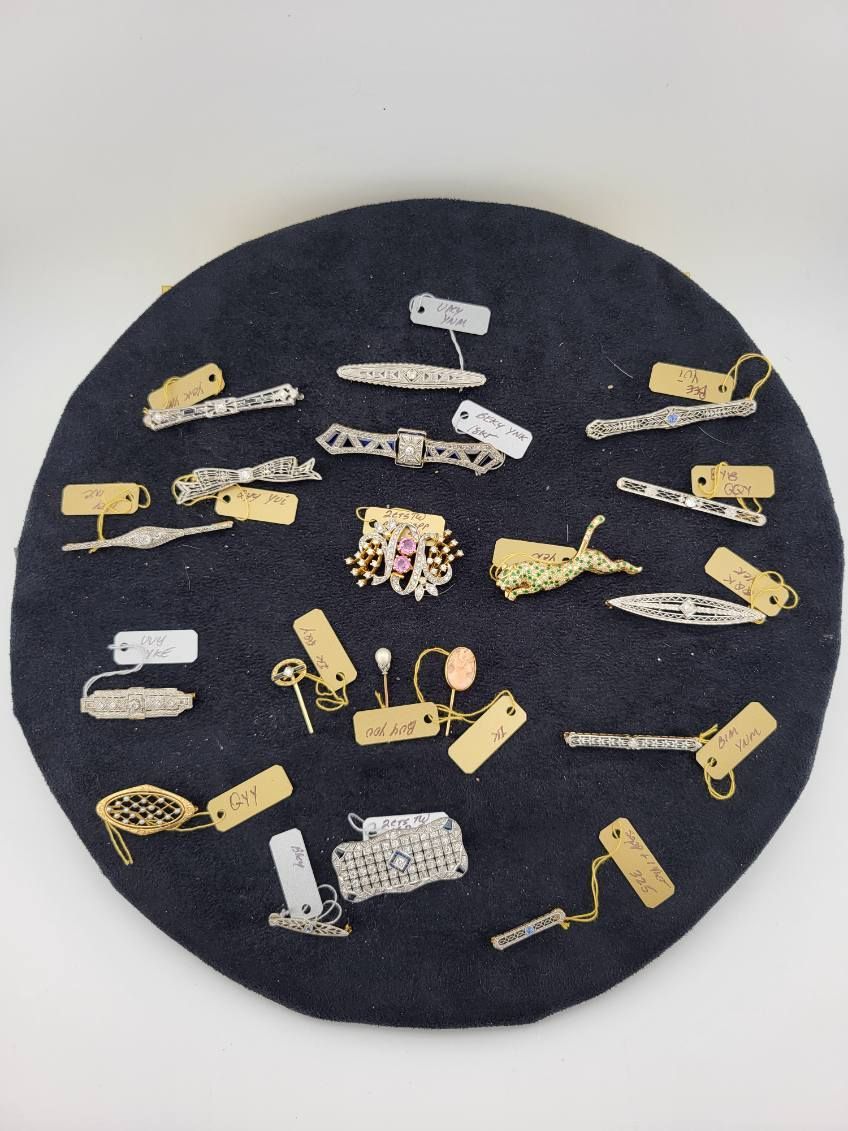 Jewelry display: rings, necklaces, bracelets, earrings with diamonds and red gemstones on red velvet, pink lace, and white cherub statues.