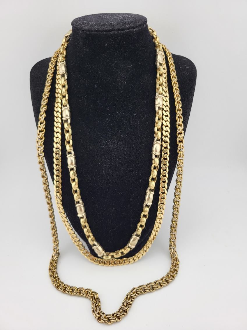 Three gold-colored necklaces draped on a black jewelry display stand.