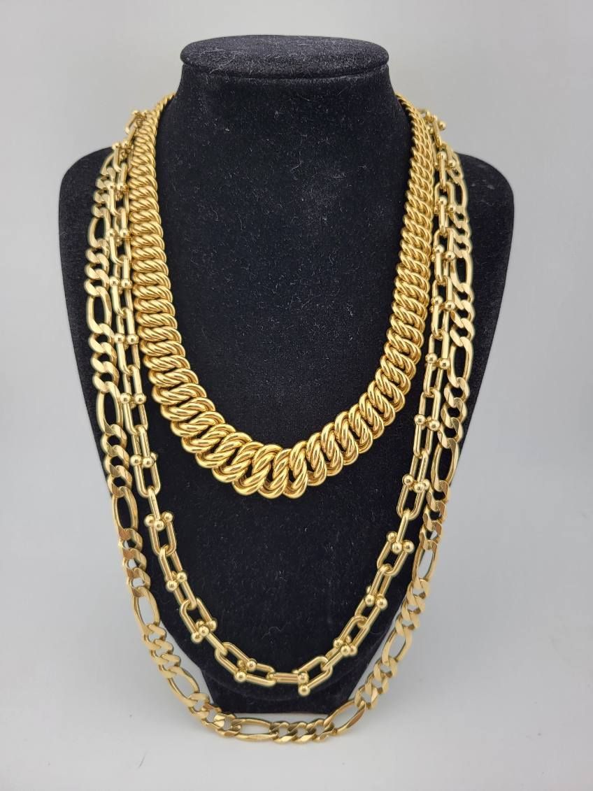 Three gold necklaces on a black jewelry bust.
