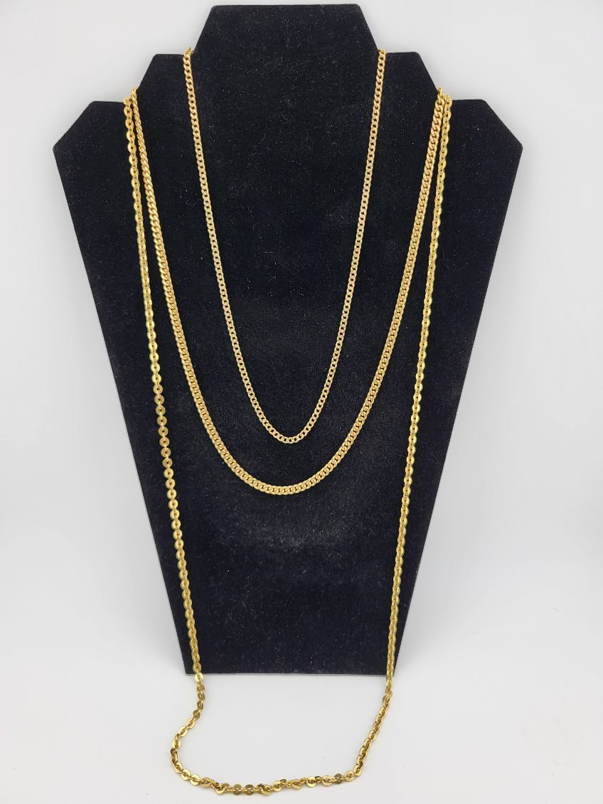 Three gold necklaces displayed on a black jewelry stand against a white background.