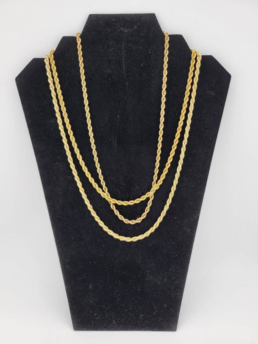 Three gold rope chain necklaces on a black jewelry display.