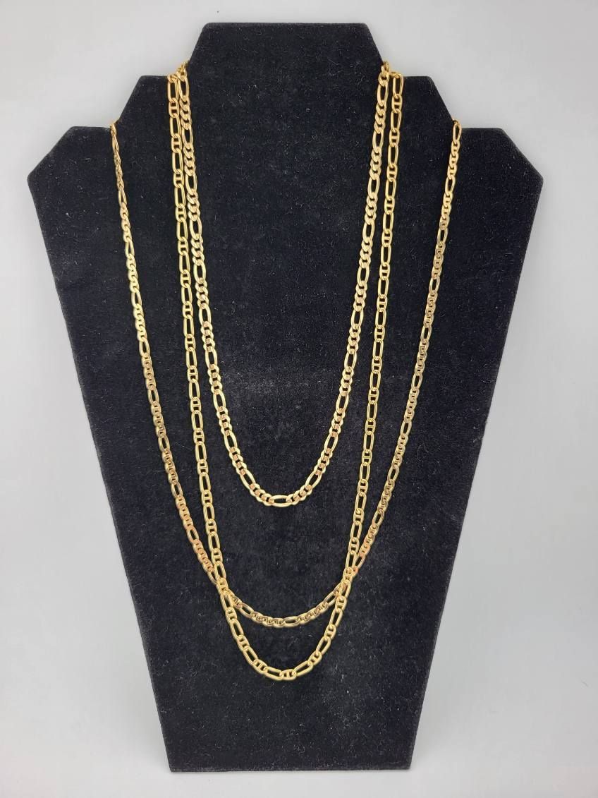 Three gold necklaces of varying lengths on a black jewelry display stand.